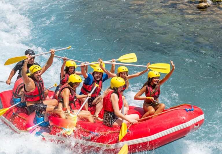 a red raft floats down the rapids of a river with 9 people in the boat having fun.  Adventure activities such as white water rafting are a great option for people traveling with PTSD.