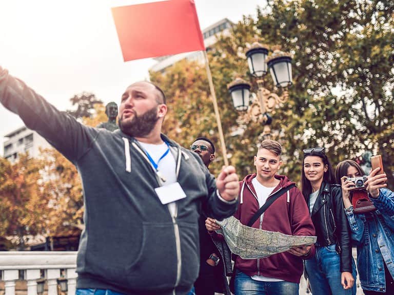 A man carrying a small red flag leads a small tour group.