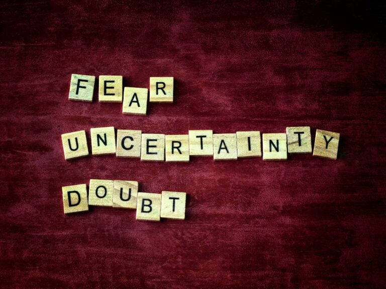 A dark red background has wooden tiles with letters on them.  There are three words made out of the tiles that say "fear, uncertainty, Doubt"