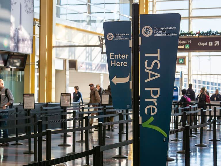 Roped lines lead to the security check point at an airport.  A blue banner says TSA Pre check.