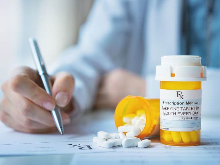 A doctor writes a prescription with two orange medication bottles to his left that contain white pills.