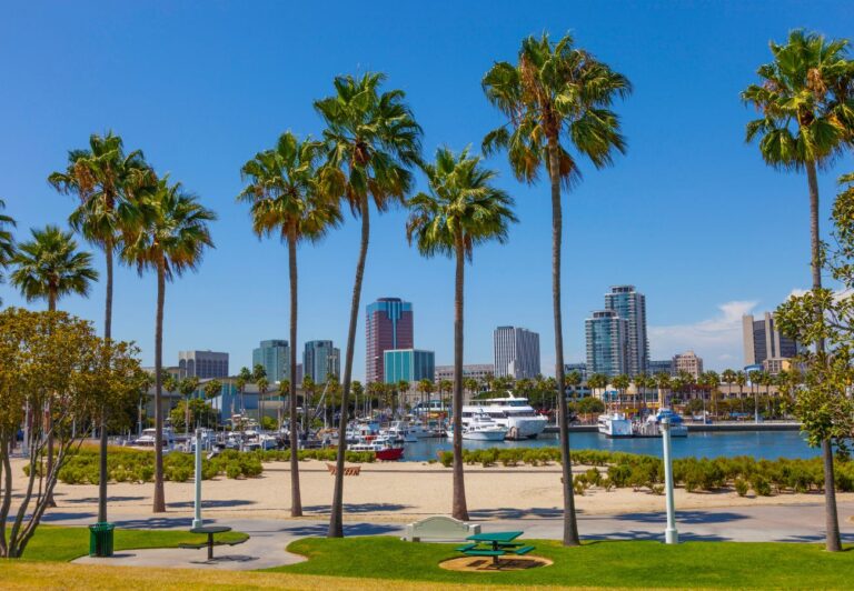 Long Beach California has paved paths around a sandy beach with the city skyline in the background.