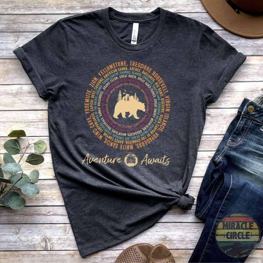 A dark grey woment's t-shirt has a bear graphic in the center of a circle which has names of national parks creating the circular design.