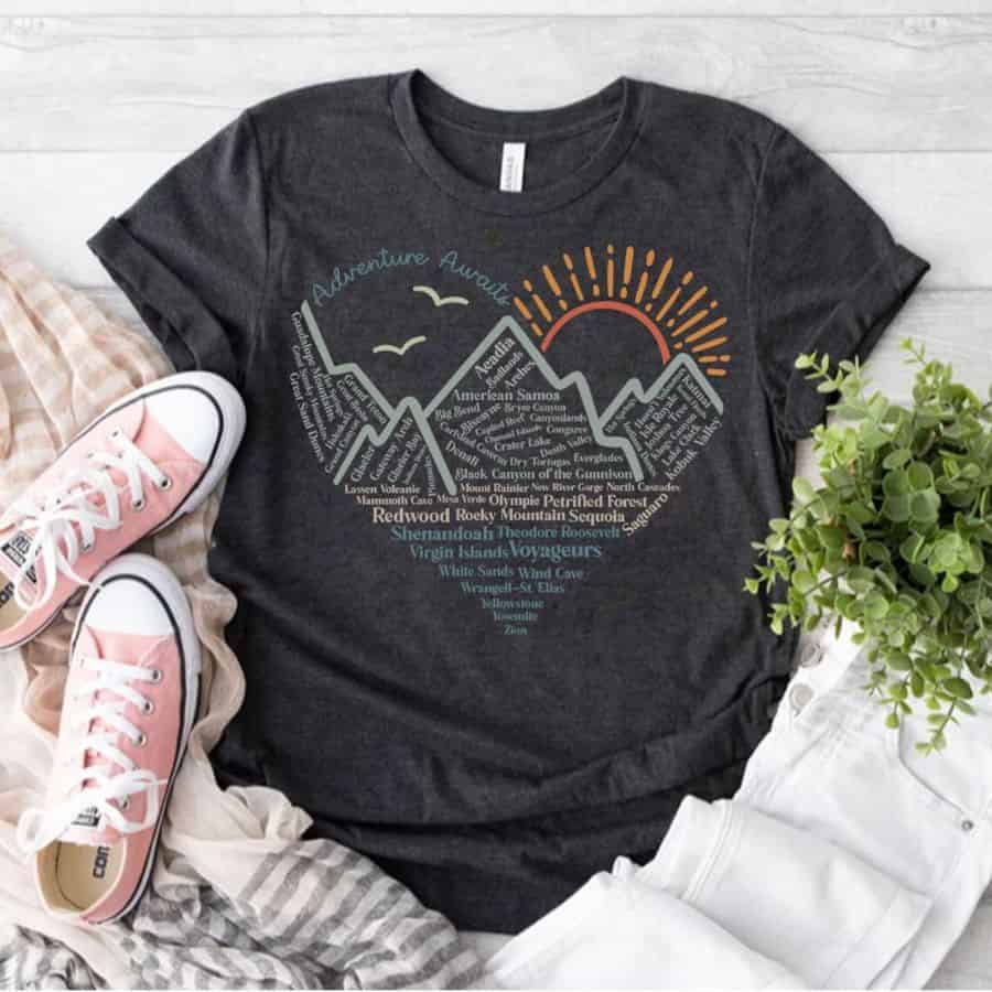 The teton mountain range with the sun rising over them is in the shape ofa heart and on a dark grey t-shirt.