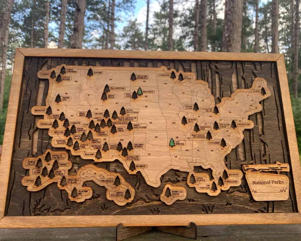 A framed wooden map of the United States with pine tree cutouts marking the spots of the US national parks.