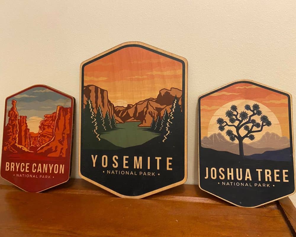 Three wooden signs depicting famous views within Bryce Canyon, Yosemite, and Joshua Tree national parks.