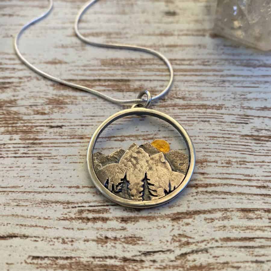 A round necklace depicts mountains from Yosemite National Park with the sun setting over top of them.