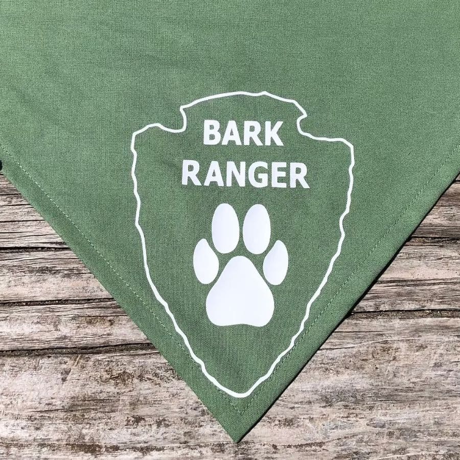 A green bandana for dogs has a white paw print with the words "Bark Ranger" above it.