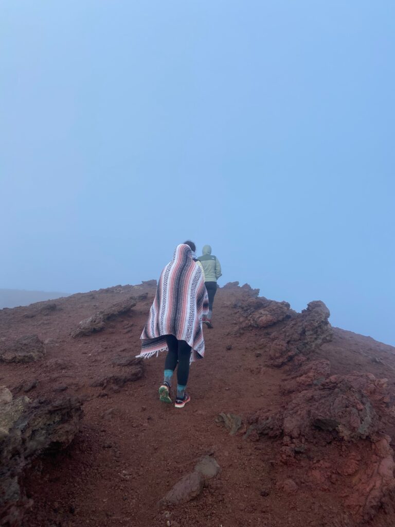 Two women are bundled up as they hike up a red dirt path in Haleakala National Park.  Make sure to add the right hiking clothes to your Hawaii packing list.