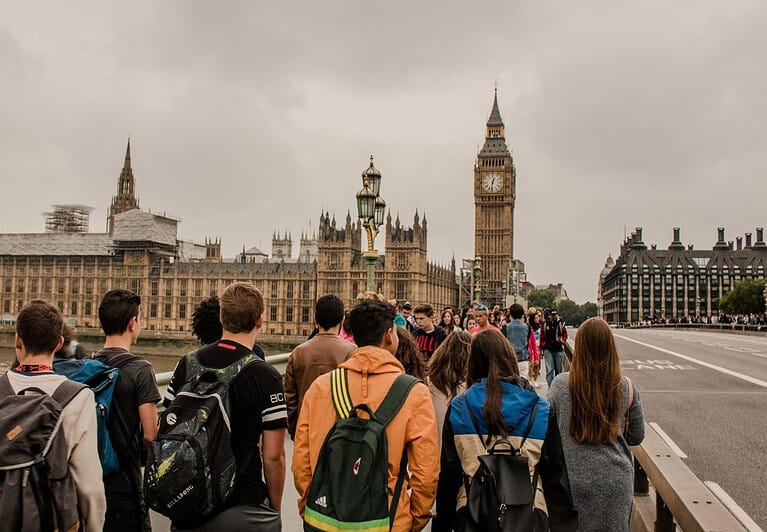 A large crowd of people is on the sidewalk leading up to the parliament building and Big Ben in London.  Summer is the worst time to visit London due to large crowds.