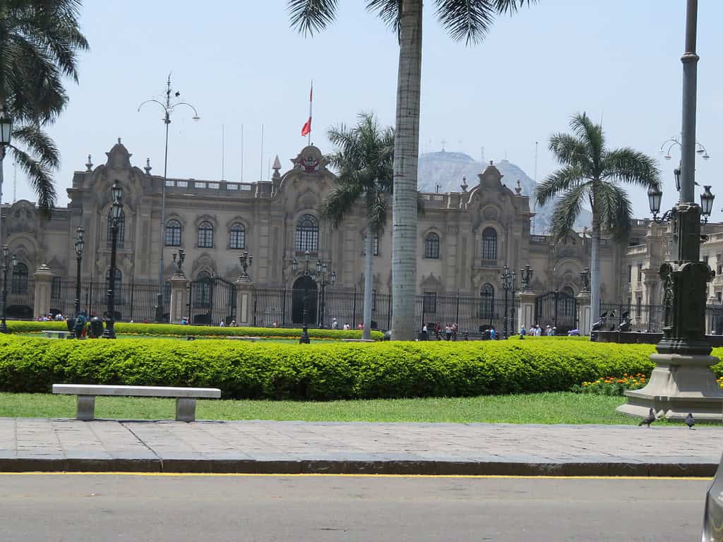 In the main square in Lima Per is a grey stone building in the Spanish Style.  Pam trees line the square in front of the building.