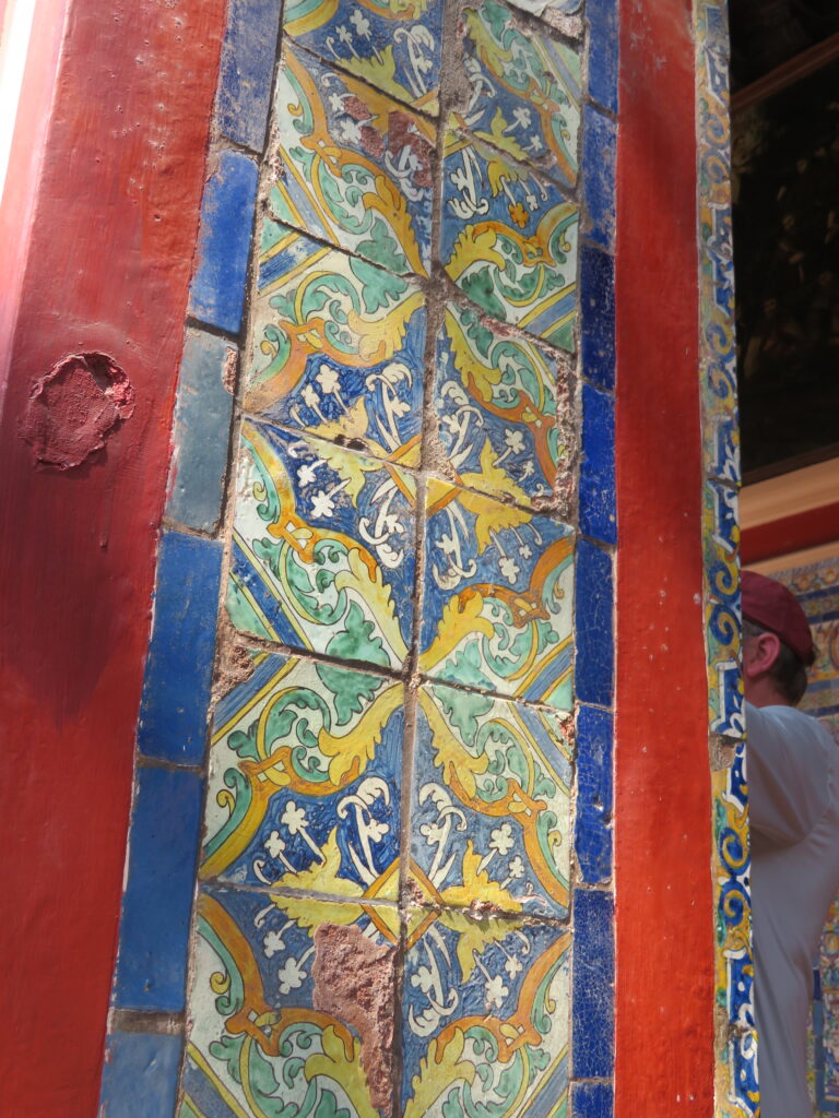 A red stone column has tile that is decorated with an intricate blue, yellow, and green pattern.