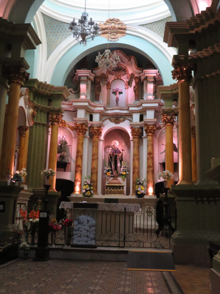 A small chapel is decorated in pinks, reds, and blues and is dedicated to a Peruvian Saint.