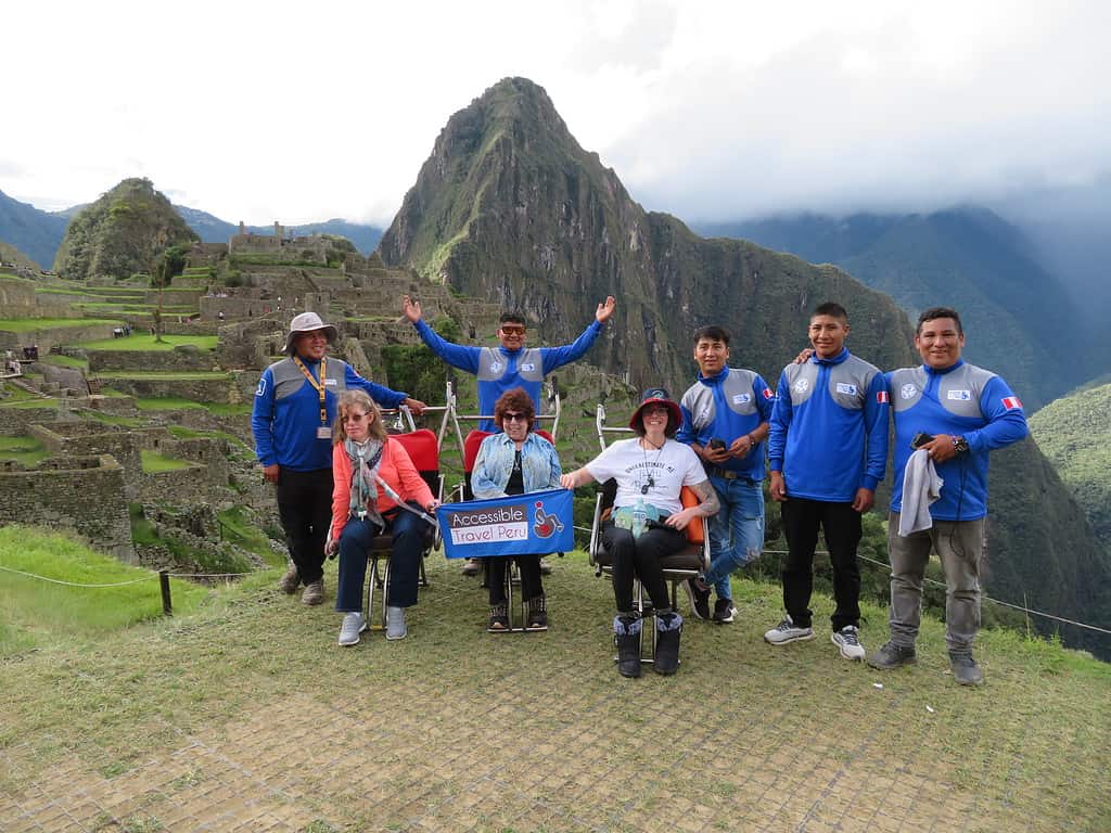 Three women in sit in adapted wheelchairs with their support staff in blue shirts behind them at an overlook in Machu Picchu Peru