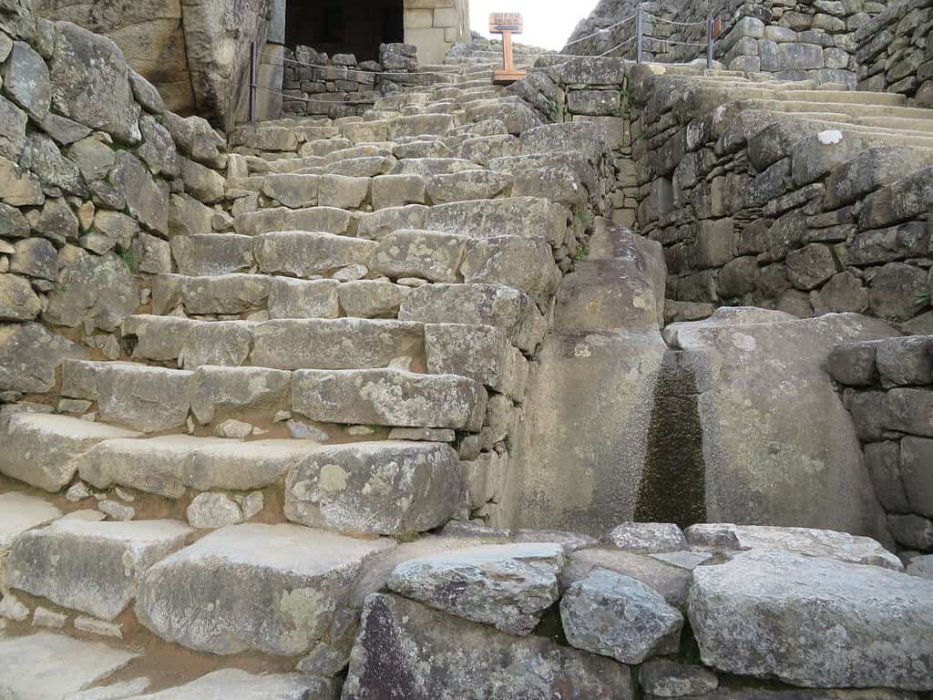 Two sets of steep stone staircases meet at the top.  In between them is a large rock with a groove on the top which directs water to the site of Machu Picchu