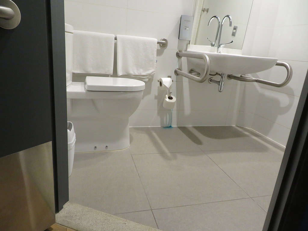 An accessible bathroom at a hotel in Peru has a toilet with a grab bar behind it and a since with grab bars on either side of it.