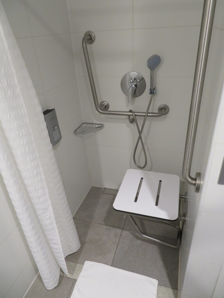 A no step shower with a fold down seat and grab bars is located in an accessible bathroom in a hotel in Peru.