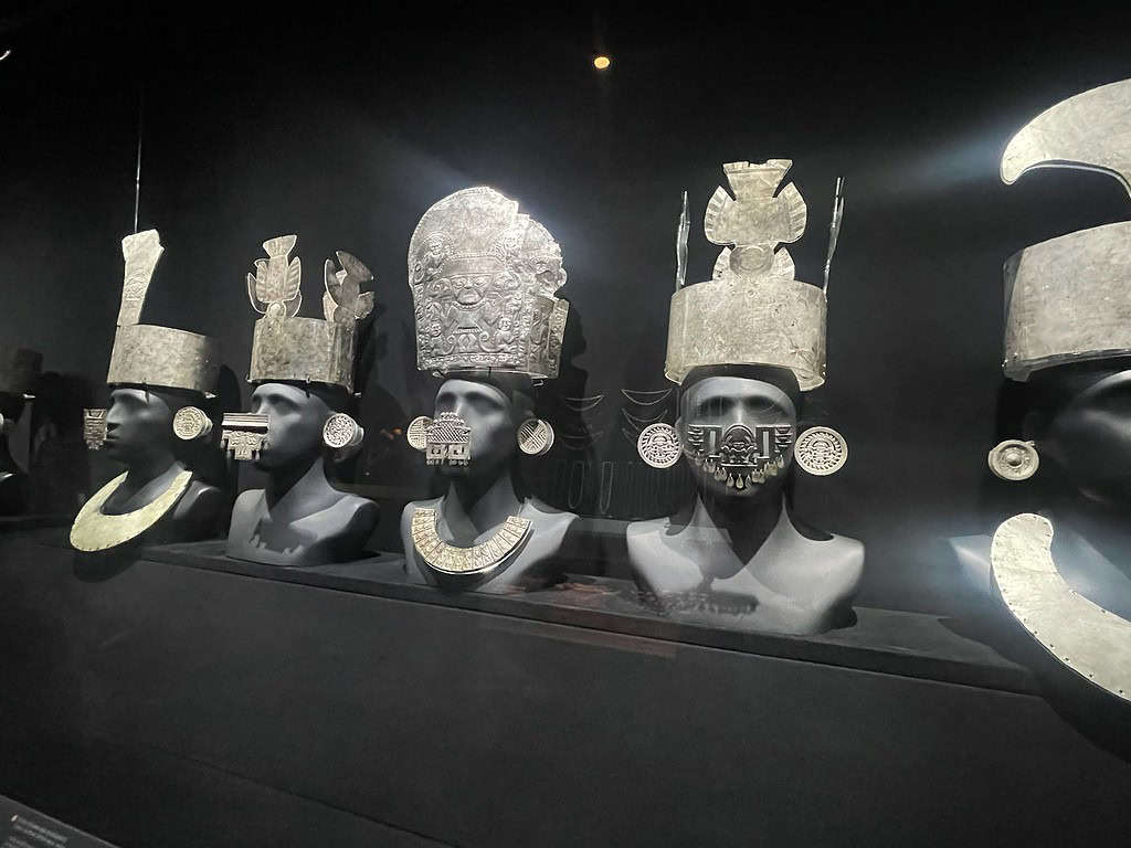 Silver and Gold jewelry and head pieces are displayed in a glass case in a museum.