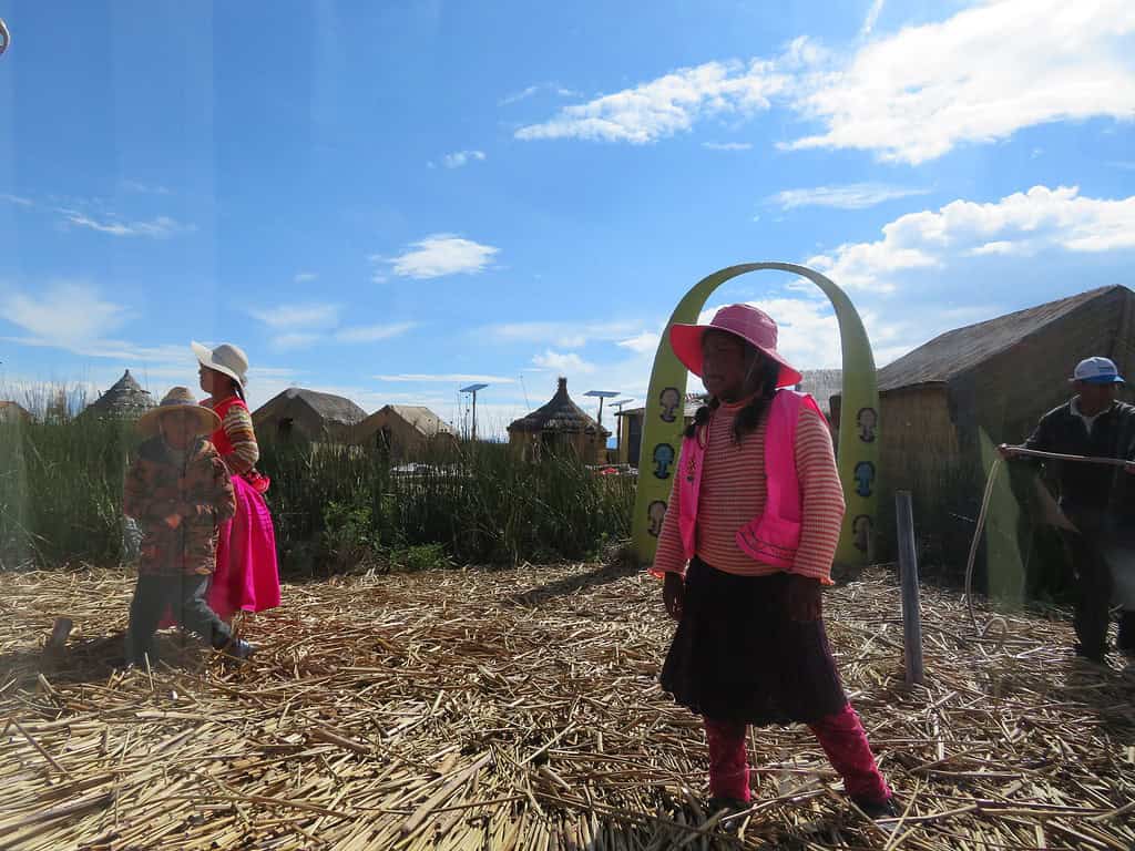 A woman and a girl dressed in bright pink clothing stand on one of the floating reed islands of Uros on Lake Titcaca to welcome visitors.