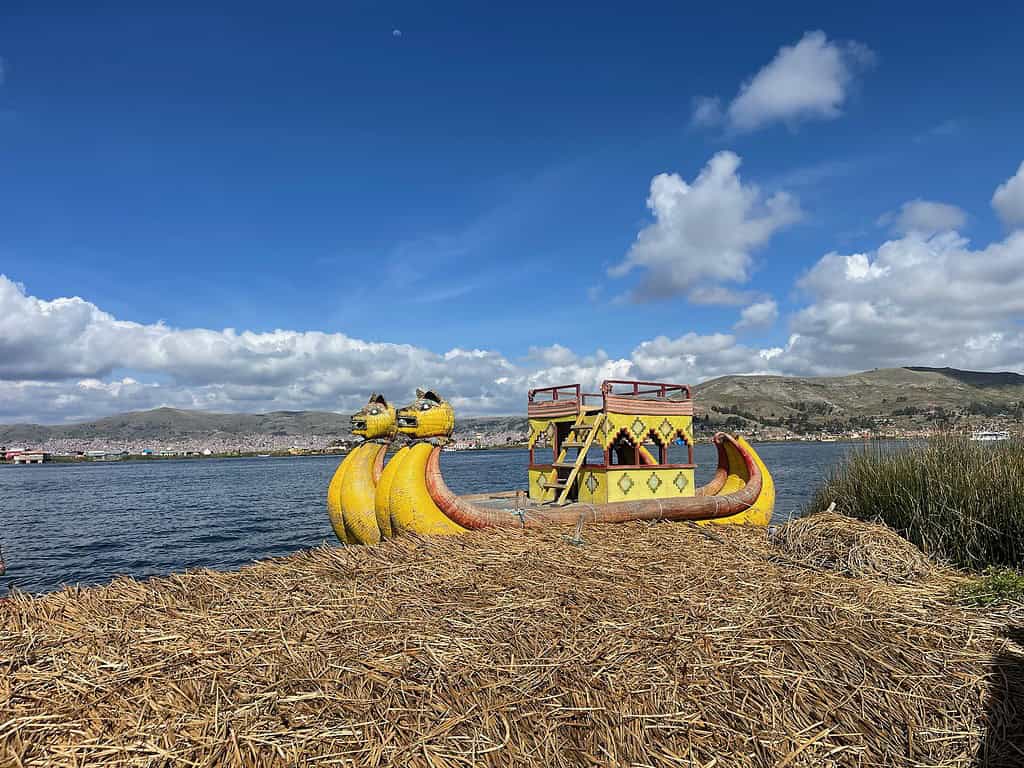 A large boat made from reeds sits on Lake Titicaca next to one of the floating islands of Uros.