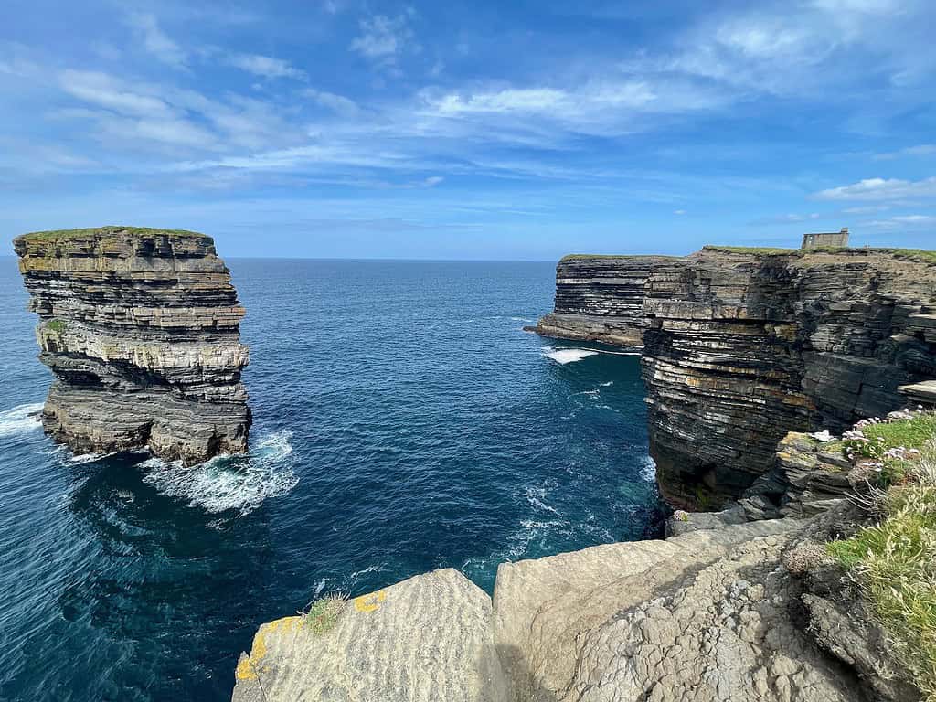 Standing along side of the tall stone cliffs at Downpartck Head you see a sea stack on the left which is separate from the cliffs which are on the right.  In the distance you can see the remains of an old World War II lookout building perched on the side of the cliffs.