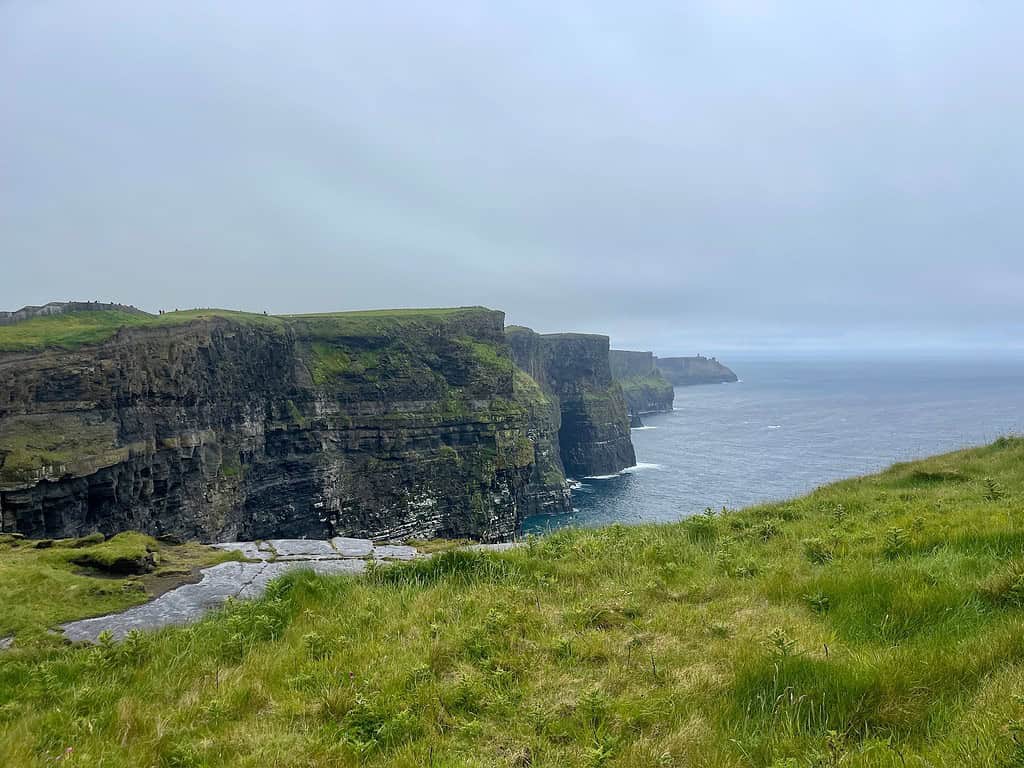 Stone cliffs with vibrant green grassy tops rise out of the sea in Ireland and are known as the Cliffs of Moher.